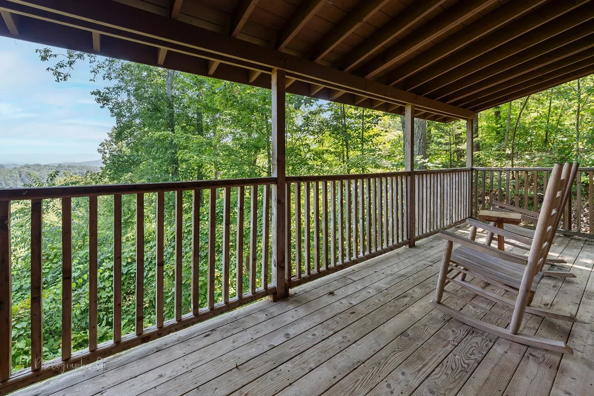 A peaceful exterior view featuring a wooden deck with classic rocking chairs and wooden railing, surrounded by lush greenery. The scene invites guests to relax outside, enjoy the fresh mountain air, and connect with nature after a day of exploring local attractions.