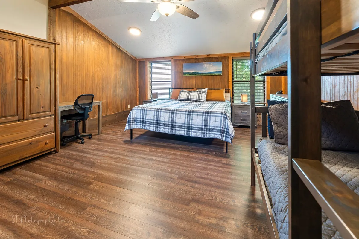 A comfortable room featuring a bed, bunk beds, a functional desk near a window, and a wooden wardrobe. The space is filled with light and designed for relaxation, work, or family gatherings, with thoughtful touches like a reading nook and workspace.