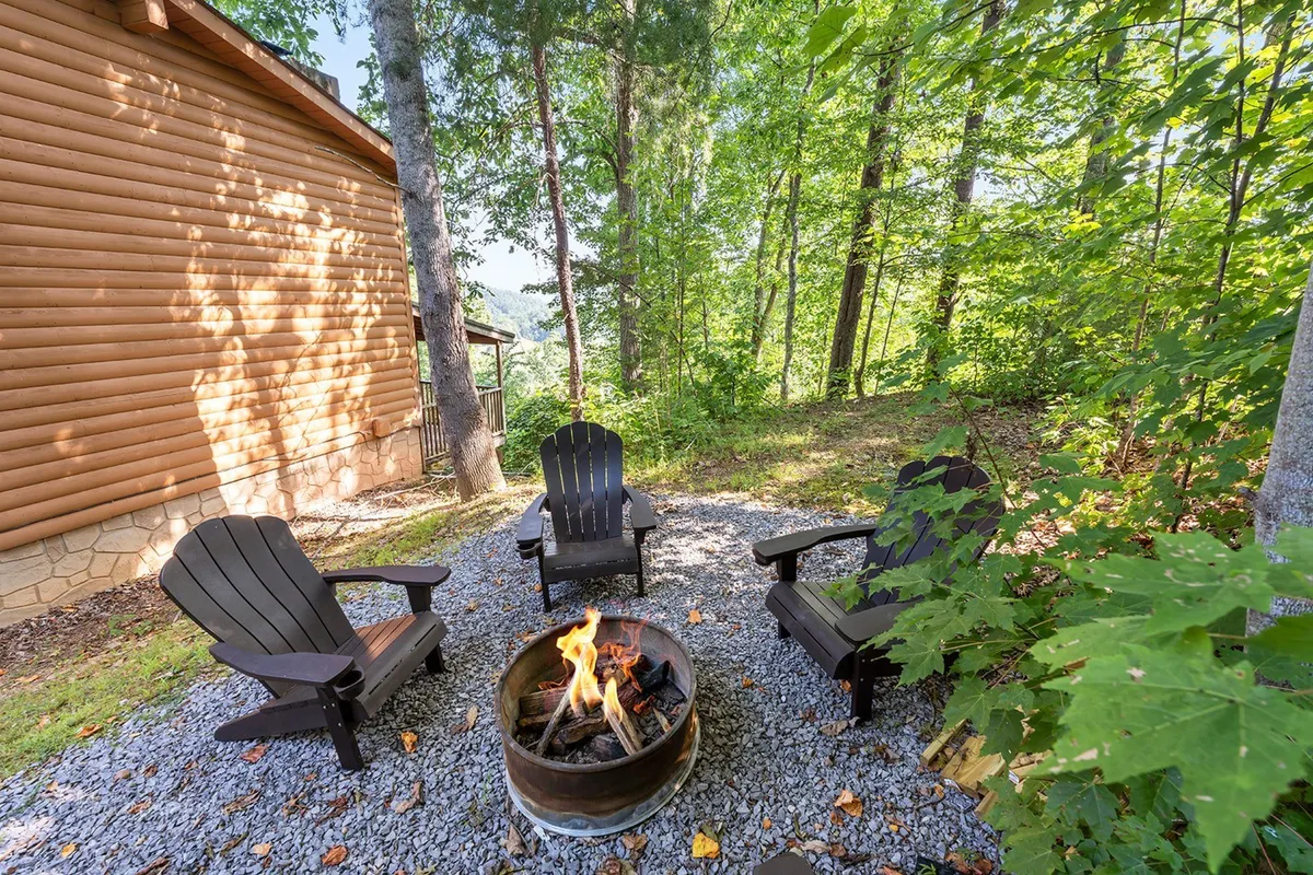 A cozy fire pit area surrounded by adirondack chairs, set amidst leafy trees. The fire pit is ready for evening gatherings, marshmallow roasting, and storytelling under the stars, perfectly complementing the outdoor experience described in the section.