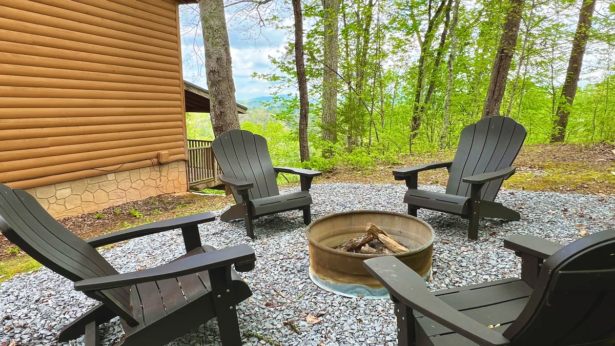 The exterior of the condo features a cozy outdoor setting with a central fire pit surrounded by inviting Adirondack chairs, nestled among tall, serene trees. The scene evokes warmth and togetherness, with guests gathered for campfire stories, making s'mores, and enjoying the peaceful Smoky Mountain atmosphere.